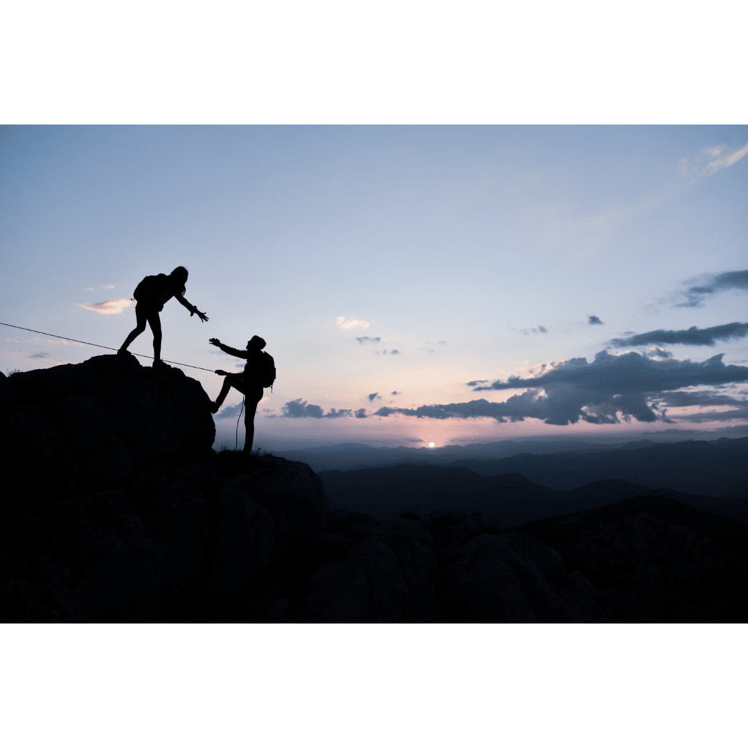 photo of two people rock climbing, one person is reaching out and helping lift up the other person